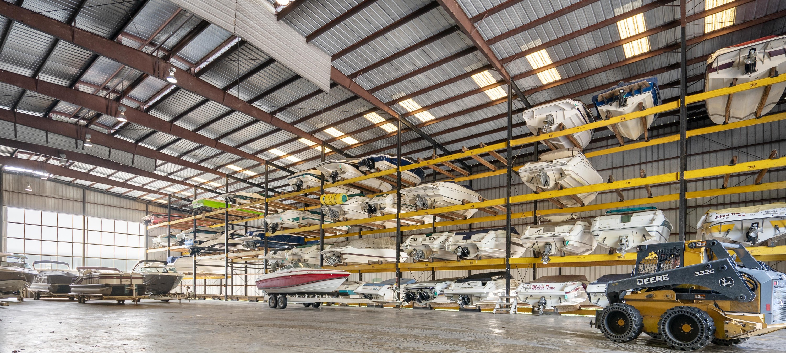 A number of boats stored on some racks in a giant warehouse with boat lift machinery nearby